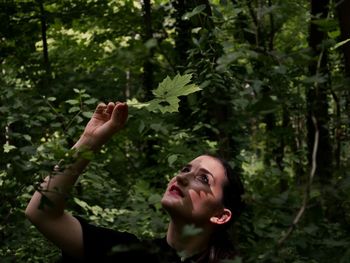 Woman holding leaf against trees in forest