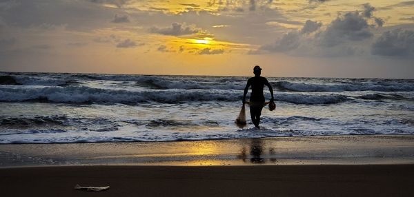 Full length of man standing on beach against sky during sunset