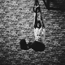 Full length of shirtless man hanging against brick wall