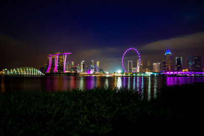 Illuminated city by river against sky at night