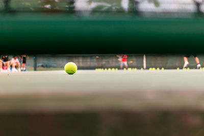 Ball on tennis court seen through railing