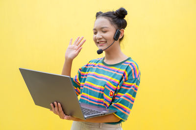 Mid adult woman using mobile phone against yellow background