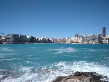 Sea by buildings against clear blue sky