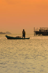 Silhouette man in boat on sea against clear sky during sunset