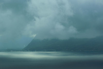 Scenic view of sea and mountains against storm clouds