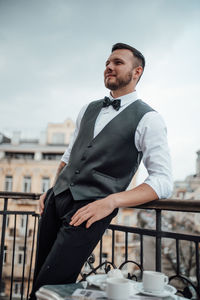 Young man looking away while standing against sky