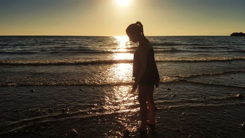 Side view of girl standing at beach during sunset