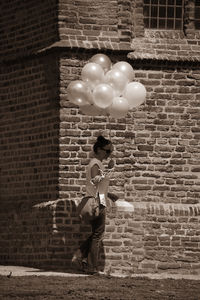 Full length of woman holding balloons while walking by old building