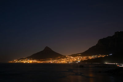 Illuminated city by sea against clear sky at night