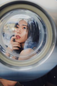 Thoughtful young woman seen through washing machine glass