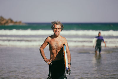 Portrait of shirtless man standing at beach against sky