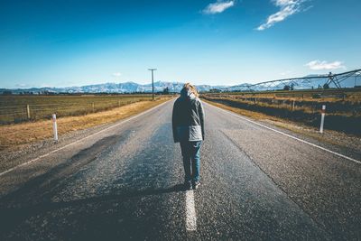 Man walking on road against blue sky