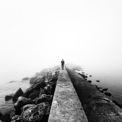 Distant view of man walking on pier in sea during foggy weather