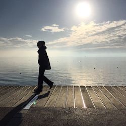 Silhouette man walking on boardwalk at shore against sea and sky