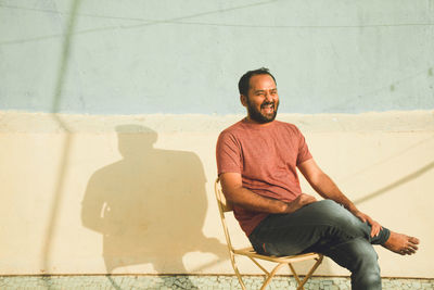 Happy man sitting on chair against wall