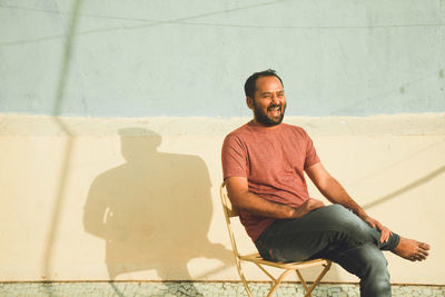 Portrait of smiling young man sitting against wall