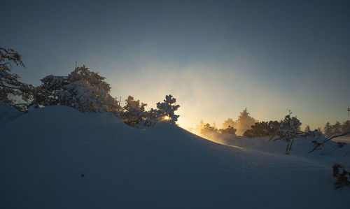 Snow covered landscape against sky during sunset