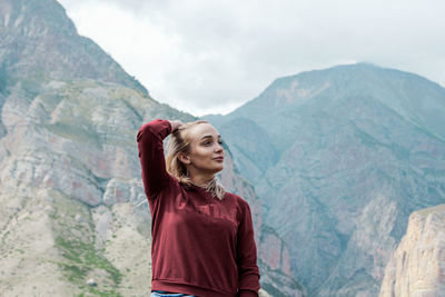 Young woman looking away while standing against mountain range