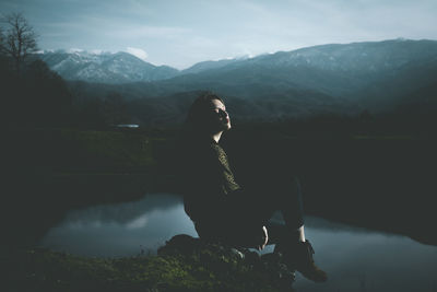 Woman sitting by lake against mountains