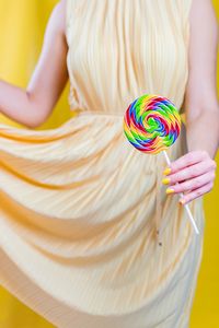 Midsection of woman holding lollipop against yellow background