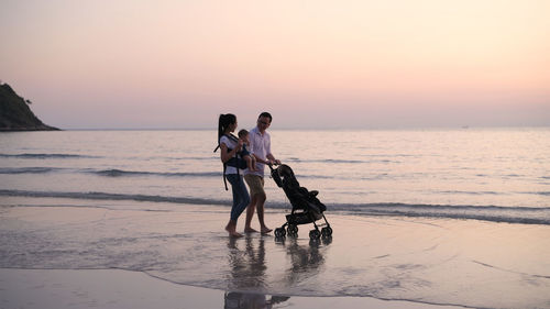 People at beach against sky during sunset