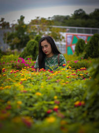 Beautiful young woman standing by flower plants