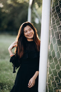 Portrait of smiling young woman standing by goal post