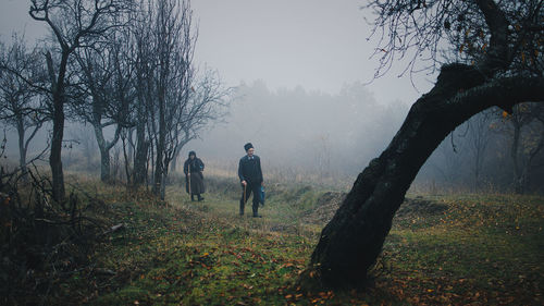 Full length of people walking on land by trees during foggy weather