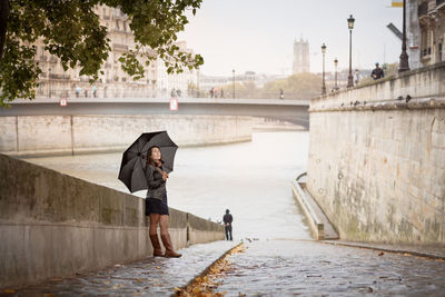 Brunette girl in a black jacket walks on the river embankment