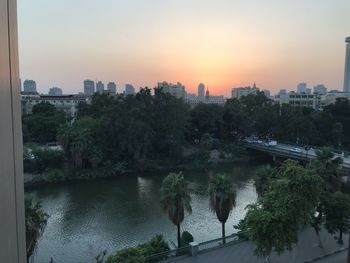 River amidst buildings in city against sky at sunset