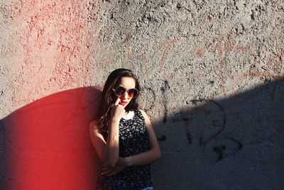 Young woman standing against wall on sunny day