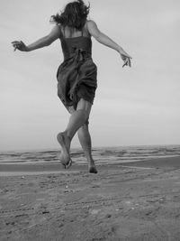 Rear view of young woman jumping on beach