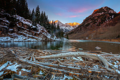 Frozen lake by trees against sky during sunset