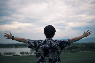 Rear view of man with arms outstretched looking at landscape against cloudy sky