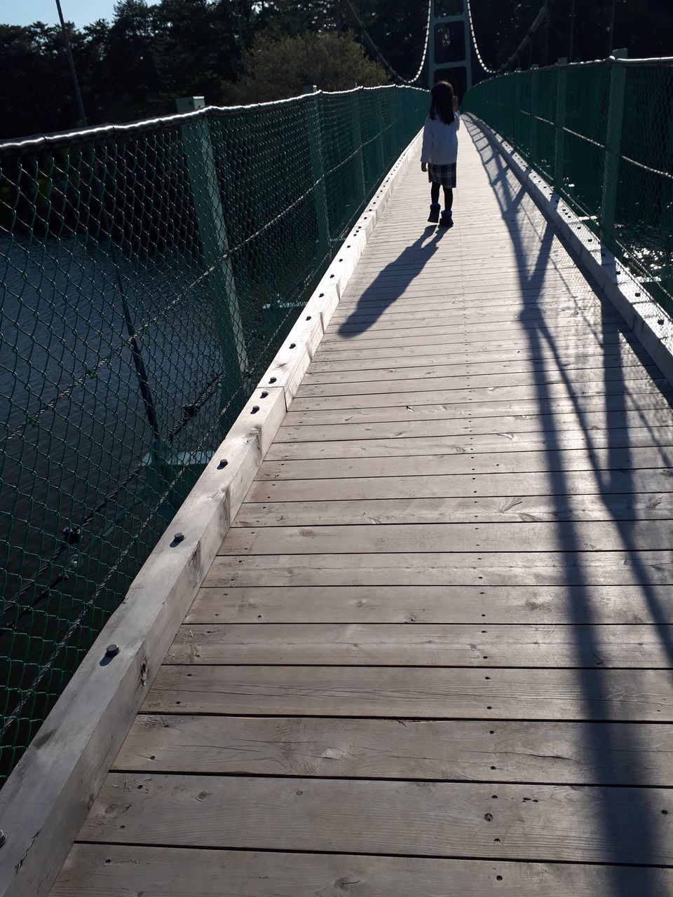 REAR VIEW OF MAN WALKING ON BRIDGE