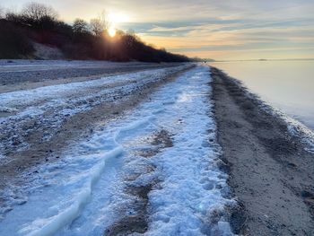 Snow covered land against sky during sunset