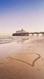 Heart sign drawn in the sand with eastbourne pier in the background