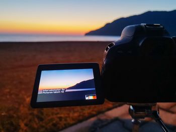 Close-up of camera on beach against sky during sunset