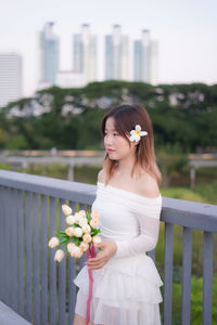 Portrait of young woman standing against railing