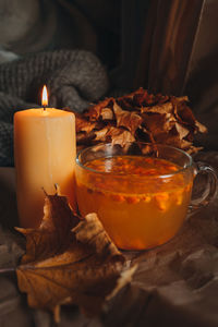 Burning candle and a mug of hot orange sea buckthorn tea in a cozy home autumn evening still life