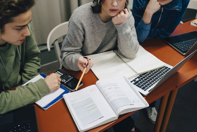 High angle view of teenage students studying while sitting with laptop at desk in school