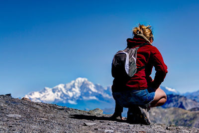 Rear view of woman crouching on mountain against clear blue sky