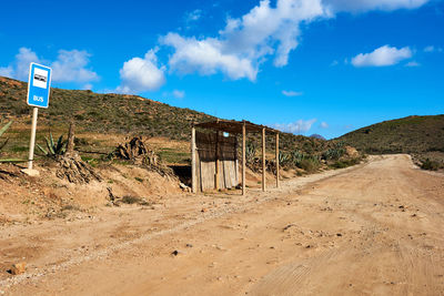 Dirt road leading towards mountain against cloudy sky