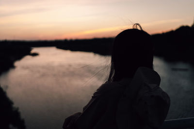 Portrait of silhouette woman looking at lake against sky during sunset