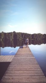 Rear view of woman sitting on pier over lake against sky