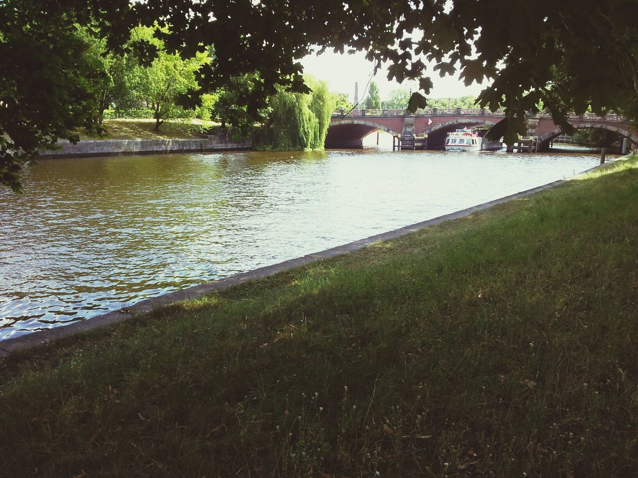 water, grass, tree, built structure, river, park - man made space, architecture, lake, reflection, nature, pond, tranquility, green color, growth, outdoors, day, riverbank, plant, building exterior, no people