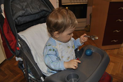 High angle view of cute boy with egg and spoon sitting on baby stroller at home