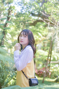 Portrait of young woman standing against trees