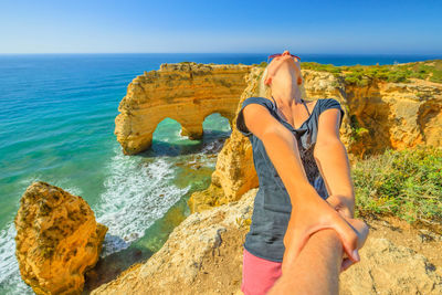 Woman holding cropped hand against sea