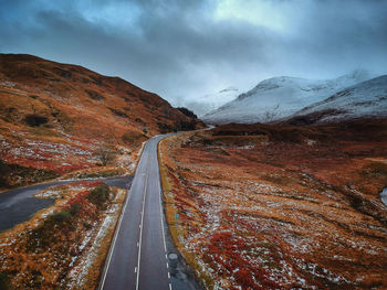 Empty road leading towards mountain against sky